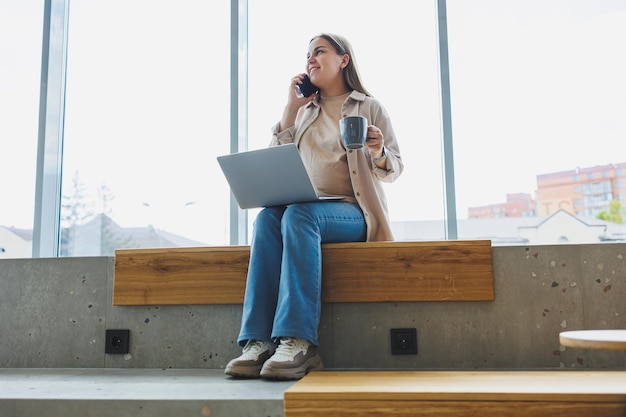 Pregnant woman sitting with laptop smartphone looking at laptop and taking notes while sitting in cafe A woman works remotely on a laptop while on maternity leave