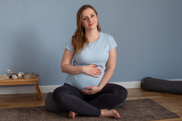 Pregnant woman sitting on yoga mat looking at camera smiling.