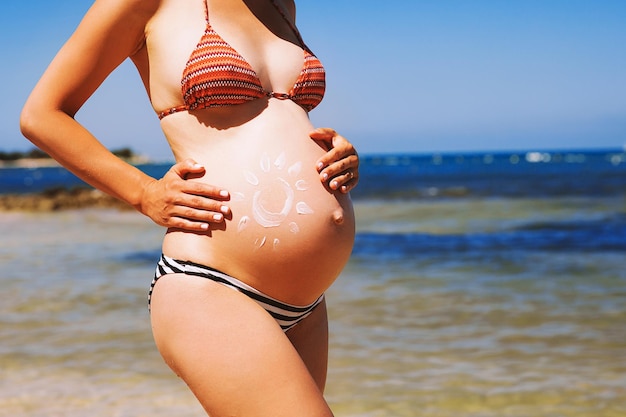 Crema idratante per la cura della pelle della donna incinta sulla pancia sulla spiaggia del mare in estate primo piano di una bella pancia incinta