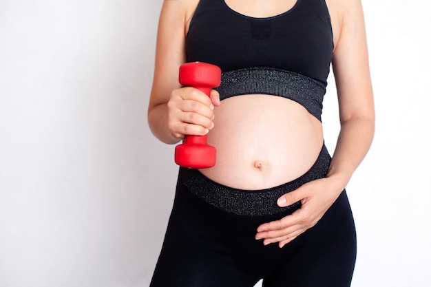 A pregnant woman in a sports uniform holds a dumbbell in her hands Sports during pregnancy