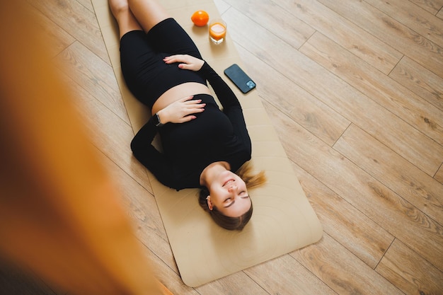 A pregnant woman in sportswear is sitting on a sports mat pregnant woman doing sports healthy lifestyle of pregnant women