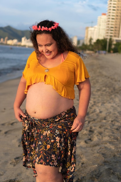 Pregnant woman standing on the beach looking at her belly