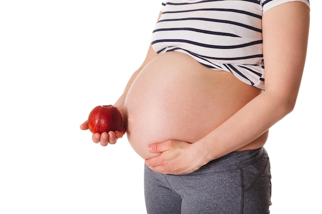 Pregnant woman standing and holding apple near her stomach