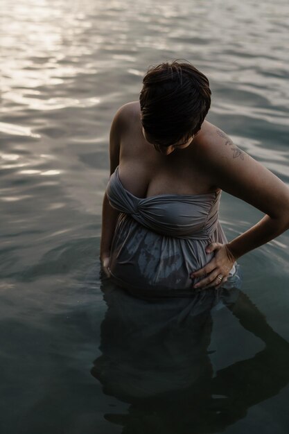Беременная женщина стоит в озере.