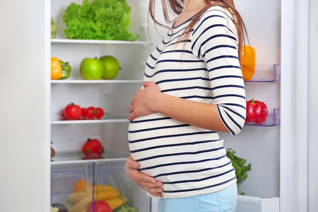 pregnant woman standing near open fridge in the kitchen