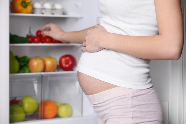 Pregnant woman standing near refrigerator full of healthy food