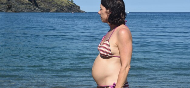 Photo pregnant woman standing sunbathing on the beach