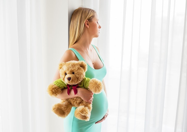 Pregnant woman standing with teddy bear