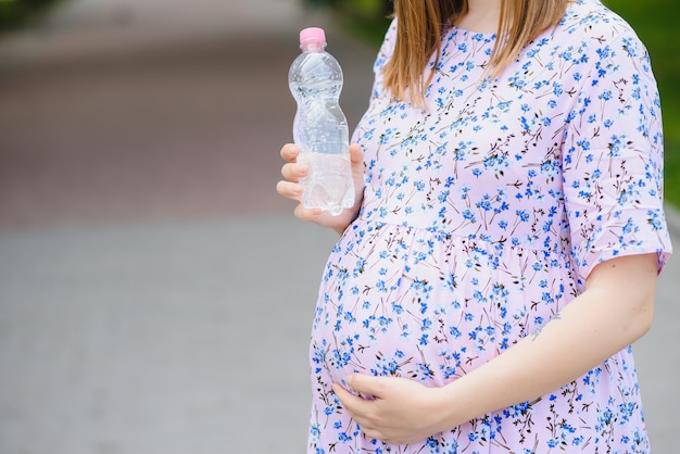 Pregnant woman stands in the park with a bottle of water