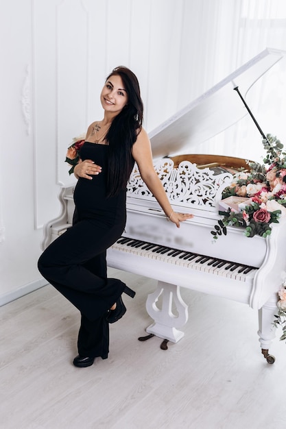 pregnant woman strokes hugging the belly tummy abdomen enjoying pregnancy standing near grand piano