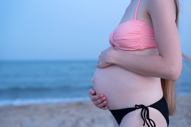 Pregnant woman in a swimsuit on the beach. Six months. Soft evening light. Belly closeup