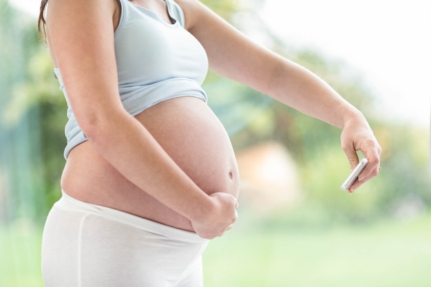 Pregnant woman taking a picture of her belly in front of a window