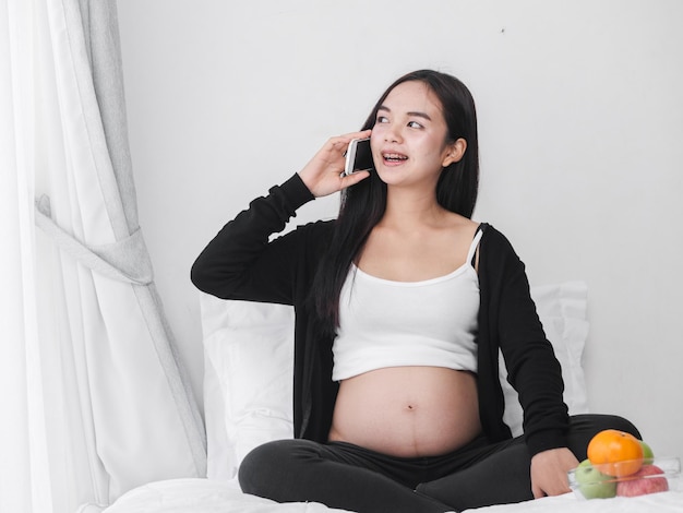침대에 앉아서 드폰으로 얘기하는 임신한 여성