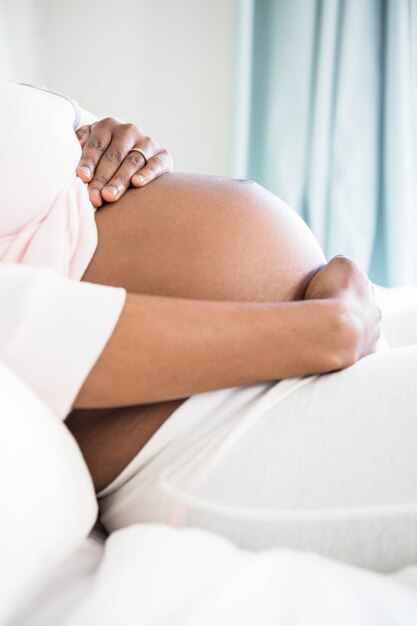 Pregnant woman touching her belly in bedroom