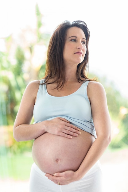 Pregnant woman touching her belly in front of a window 