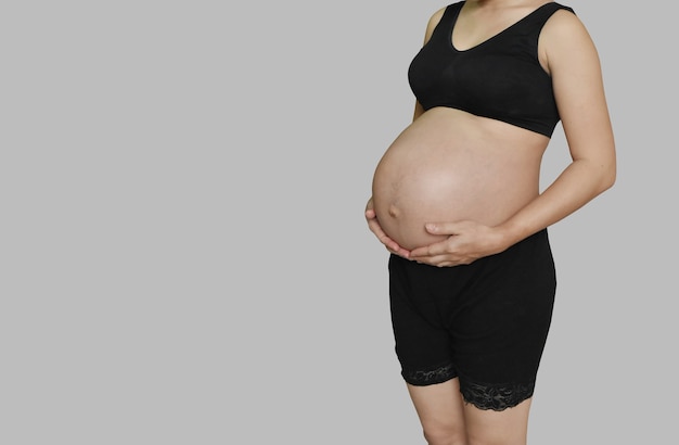 Pregnant woman touching her belly on grey background