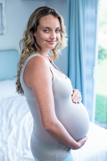 Pregnant woman touching her belly in her bedroom