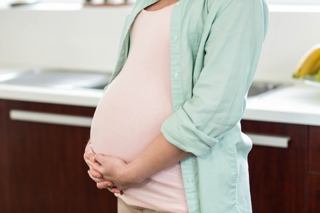 Pregnant woman touching her belly in kitchen