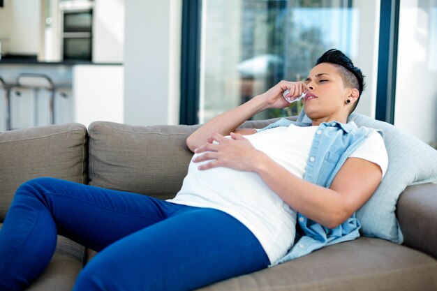 Pregnant woman touching her belly and relaxing on sofa in living room