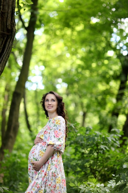 Pregnant woman touching her big belly and walking in the park relaxing in outside