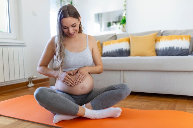 彼女の腹を愛撫するヨガを訓練している妊婦若い幸せな妊婦は、赤ちゃんのことを考えてリラックスし、彼女の将来の生活を楽しんでいます母性妊娠ヨガの概念