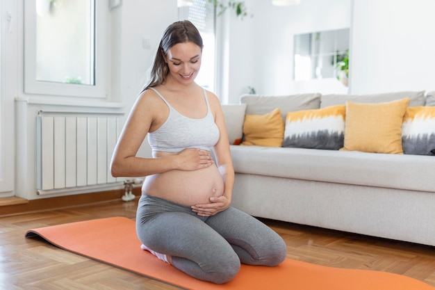 Pregnant woman training yoga in hero pose, caressing her belly.
young happy expectant relaxing, thinking about her baby and
enjoying her future life. motherhood, pregnancy, yoga concept