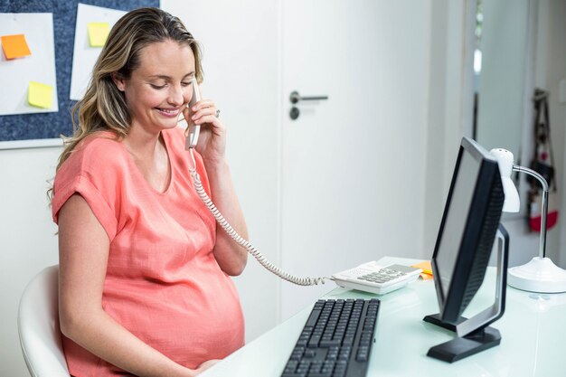 Pregnant woman using computer and phone in an office