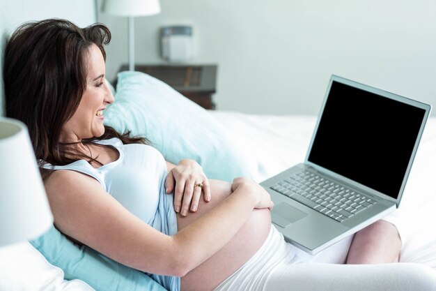 Donna incinta che utilizza computer portatile nel suo letto