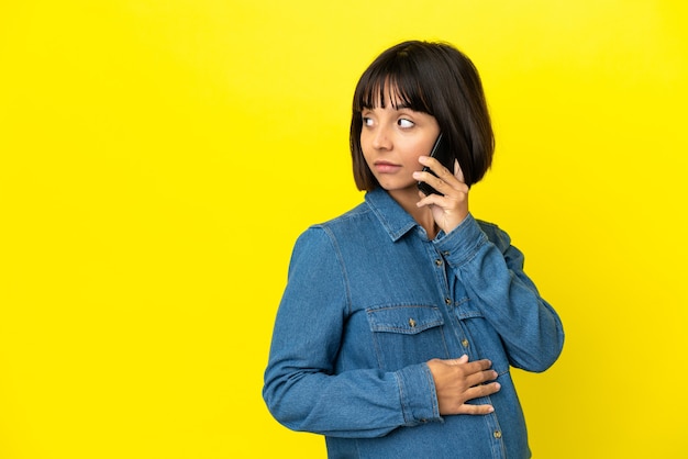Pregnant woman using mobile phone isolated on yellow background looking to the side