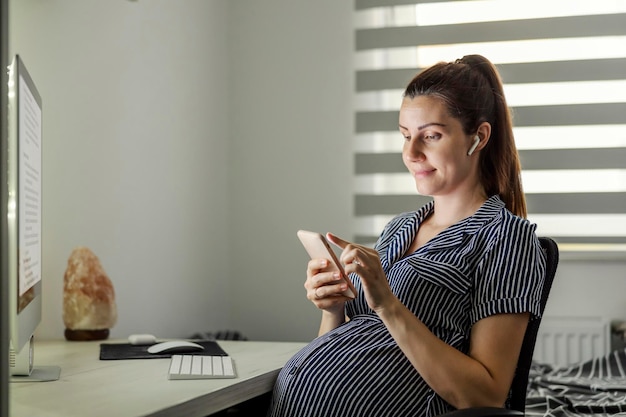 Pregnant woman using a phone at the home office