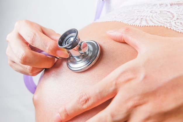 Pregnant woman using stethoscope examining on her baby in her belly