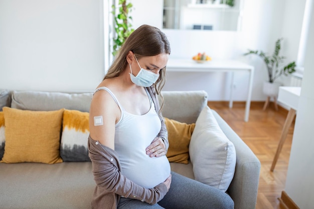 Donna incinta vaccinata contro il covid-19 che mostra il braccio con bendaggio in gesso dopo la seduta di iniezione di vaccino contro il coronavirus. sorridendo alla macchina fotografica.