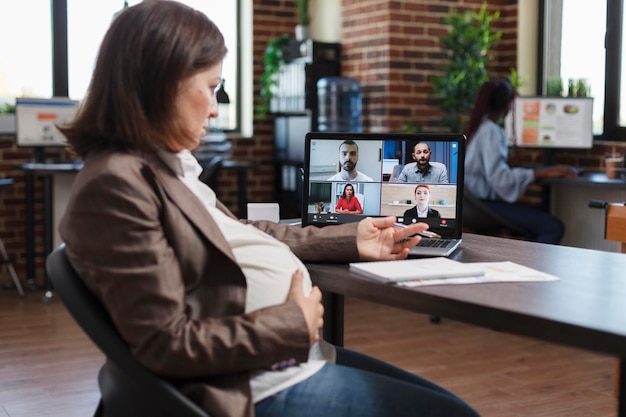 Pregnant woman on virtual conference videocall communicating marketing strategy to company partners. Financial agency employees brainstorming client oriented project ideas while in digital meeting.