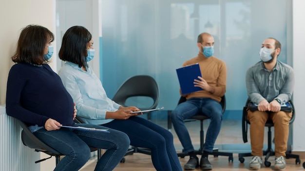 Donna incinta in attesa in coda con un gruppo eterogeneo di candidati per partecipare alla riunione del colloquio di lavoro. richiedente con pancia in gravidanza e maschera per il viso che si prepara per l'appuntamento di lavoro.