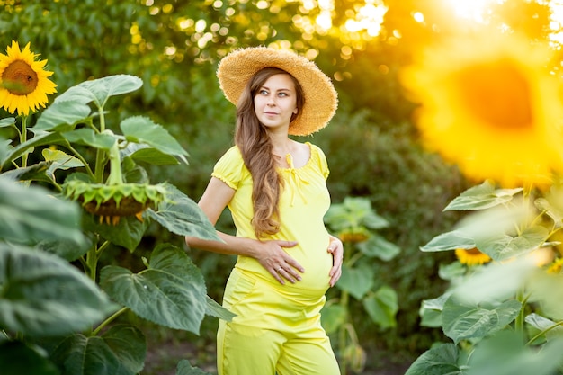 A pregnant woman walks in a field with sunflowers