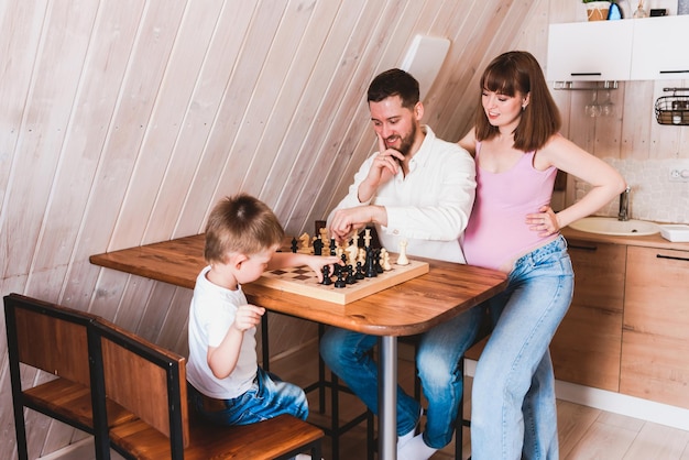 Pregnant woman watching dad and son play chess at the table