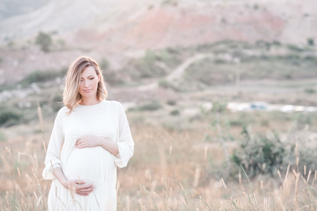 Беременная женщина в платье позирует на открытом воздухе над природой
