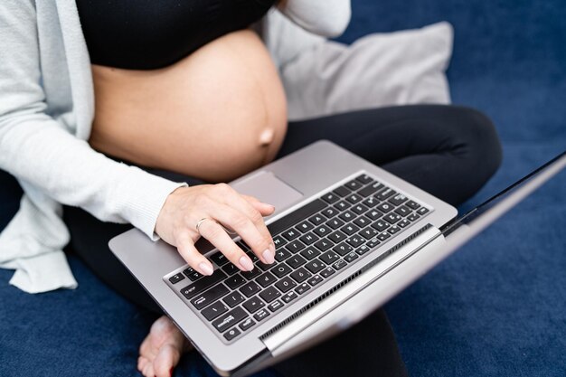 A pregnant woman wearing sports clothes sits on the couch in the living room and texting an email