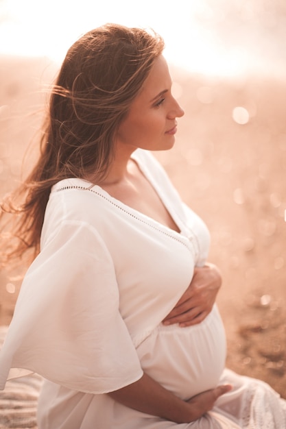 Pregnant woman wearing white dress sitting over sea