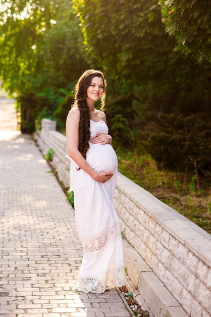 A pregnant woman in a white dress hugs her stomach