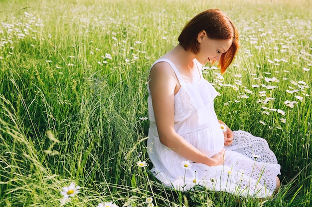 Pregnant woman in white dress on nature outdoors in a meadow Pregnancy expectation concepts