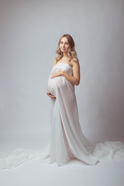 Pregnant woman in white long dress on light background