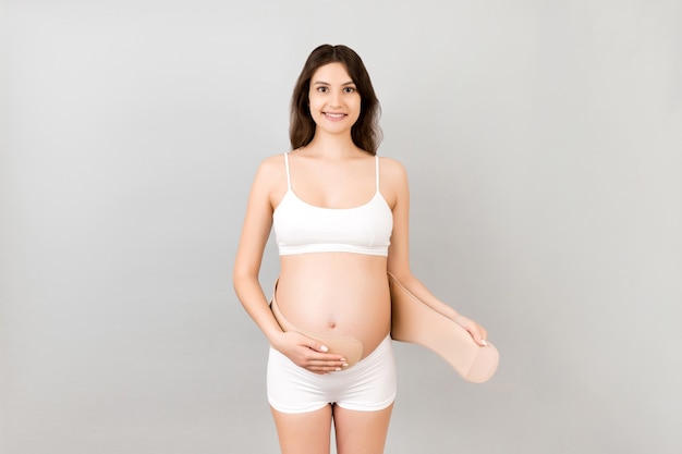 pregnant woman in white underwear putting on a bandage