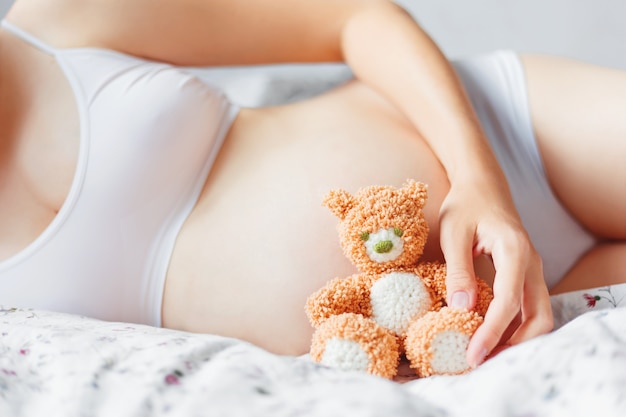 Pregnant woman in white underwear with toy bear.