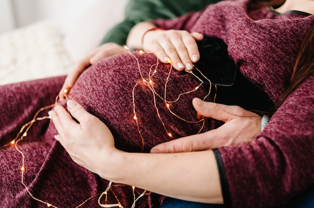 Pregnant woman whose belly is decorated with fireflies man hugs it New Year and Merry Christmas