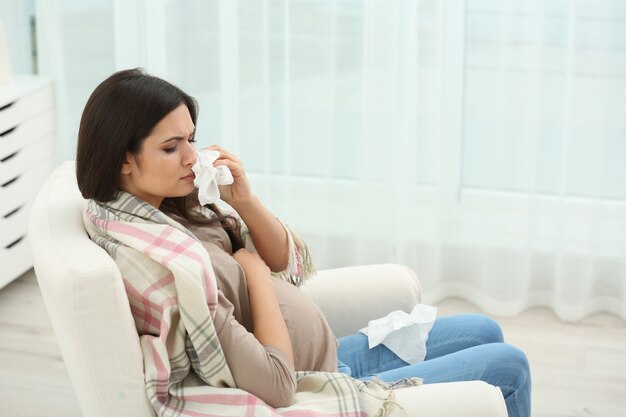 Pregnant woman with allergy sitting on armchair at home