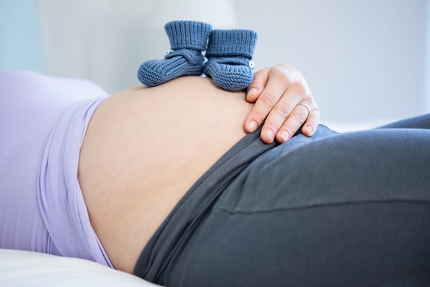 Pregnant woman with baby shoes on belly at home