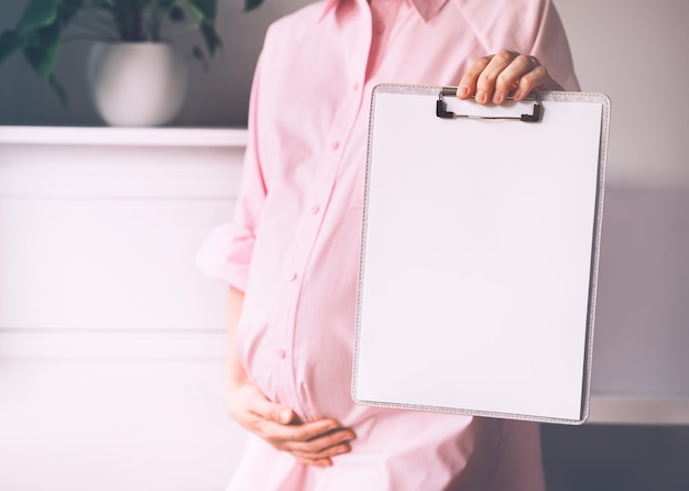 Donna incinta con carta bianca vuota come carta medica accordo vuoto concetto di firma contratto di vaccinazione carta di lavoro scrittura piano di nascita controllo sanitario durante la gravidanza modello per testo