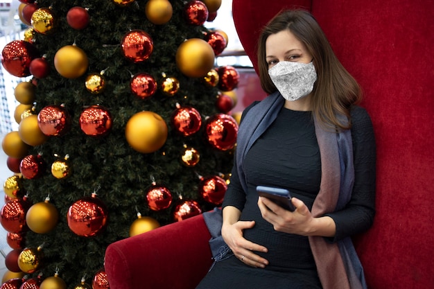 屋内でフェイスマスクのテキストメッセージを持っている妊婦