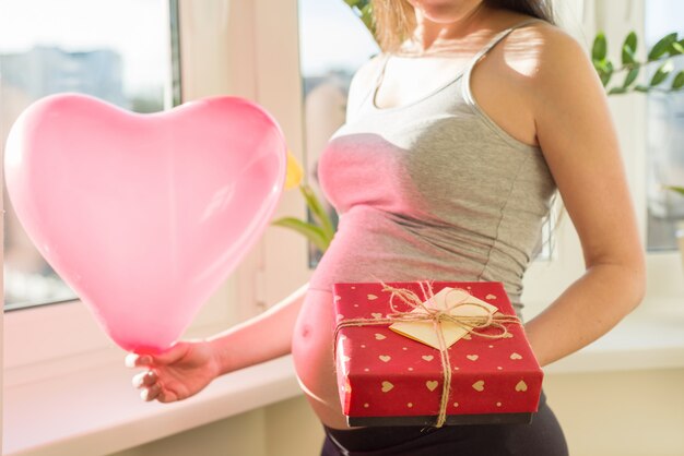 ギフト用の箱とピンクのハートのバルーンと妊娠中の女性